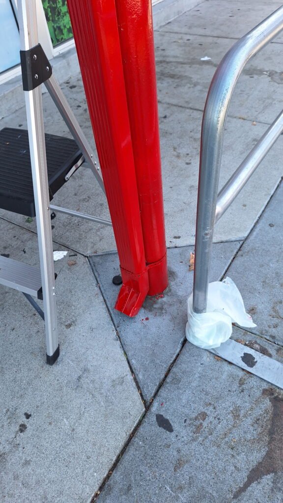 Red downspout sections next to a step ladder on a San Francisco sidewalk