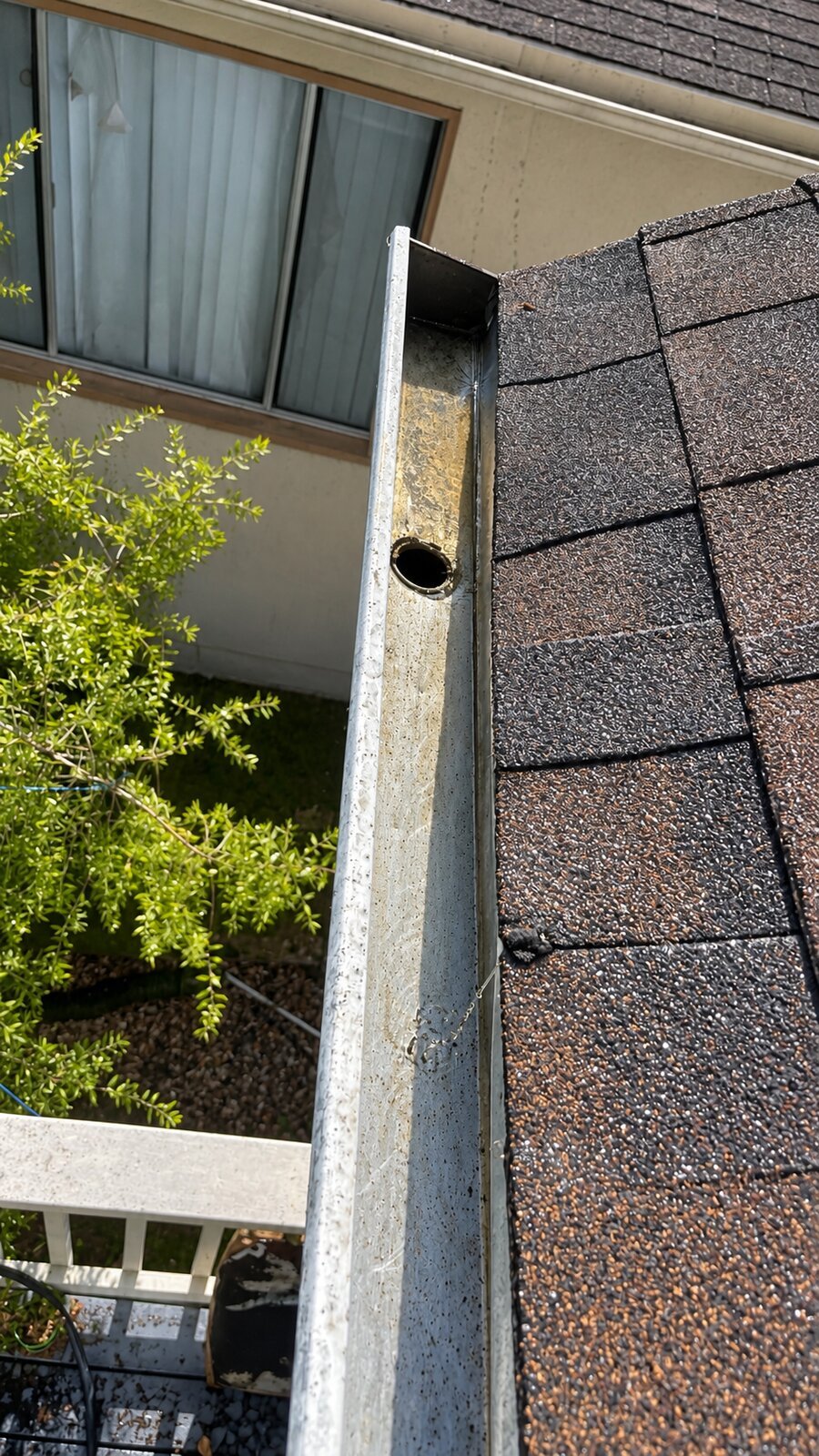 Clean metal gutter with open downspout outlet next to a shingle roof in San Francisco